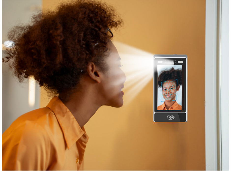 a woman smiling looking at a mounted phone system that is putting out a glow of white light and reproducing her face on the screen