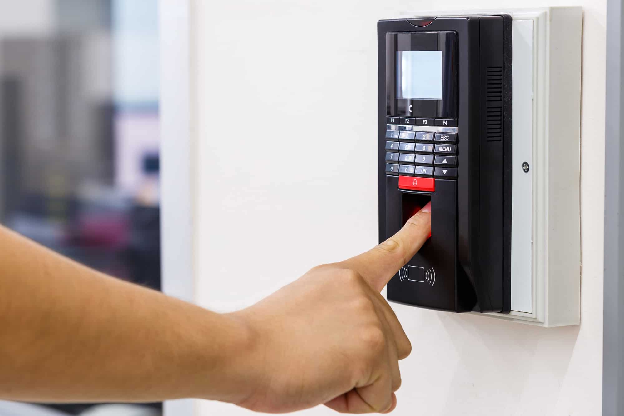 a biometric time clock against the wall as a hand puts its finger onto the clock in space