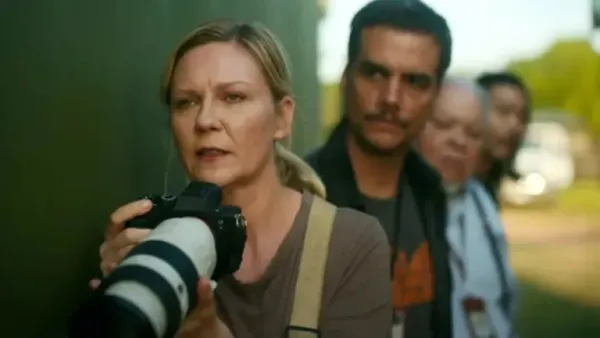 a screen from Civil War, with Kirsten Dunst holding a telephoto camera as three other characters stand behind her