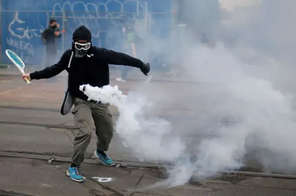 A protestor in gas mask and goggles swings a tennis racket to hit back a tear gas cannister bouncing in the air